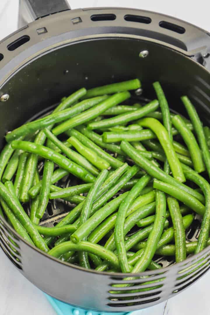 green beans seasoned in air fryer basket.