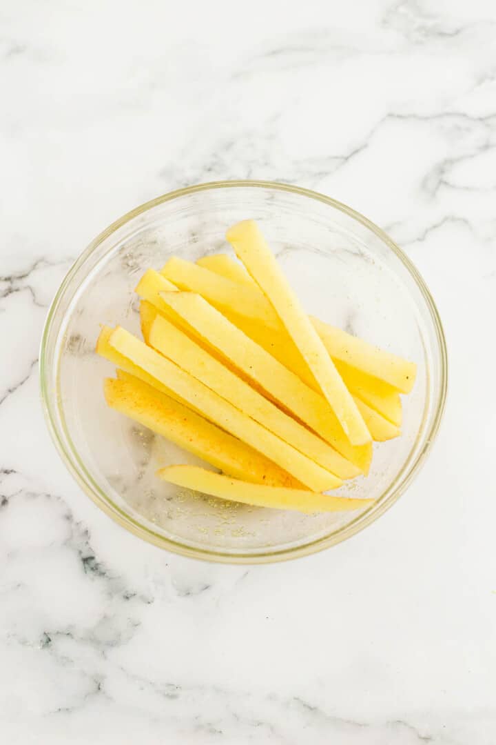 seasoning French fries in a glass bowl.