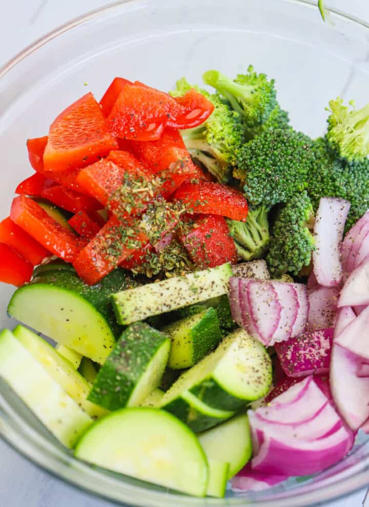 adding seasoning to the veggies in the glass bowl.