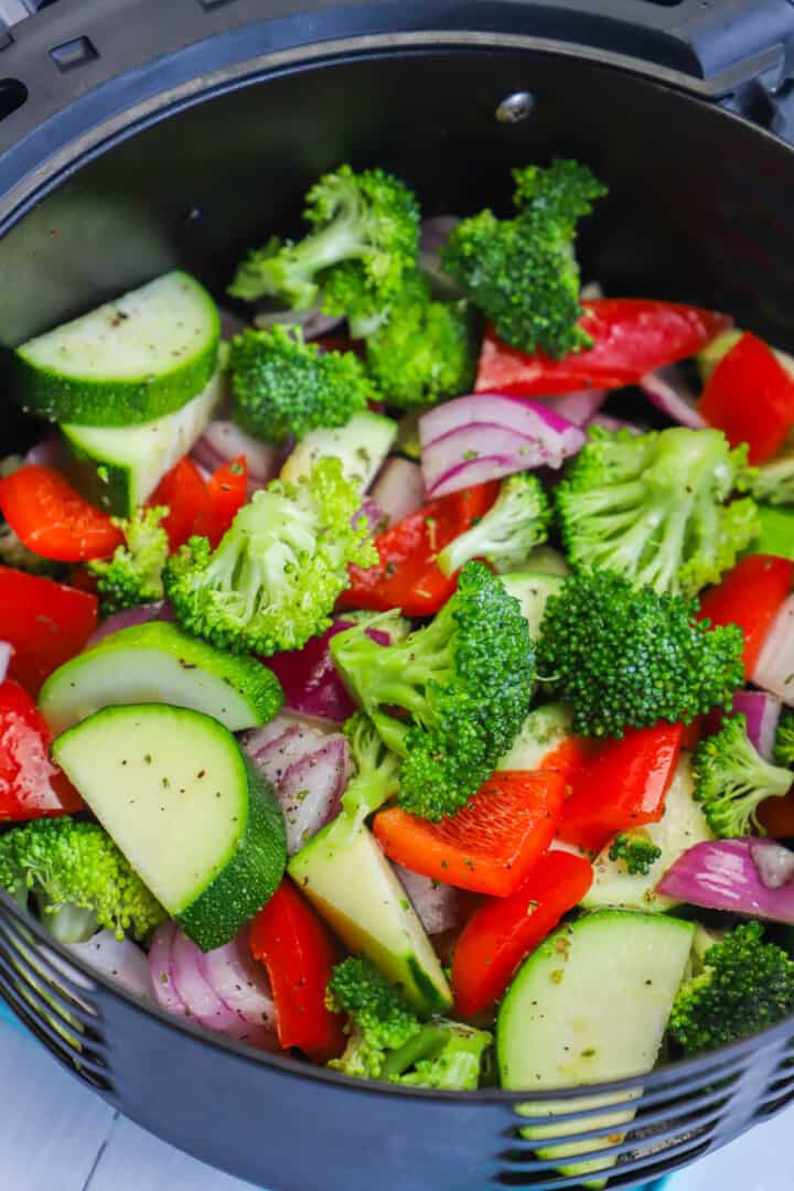 adding seasoned veggies to the air fryer tray.