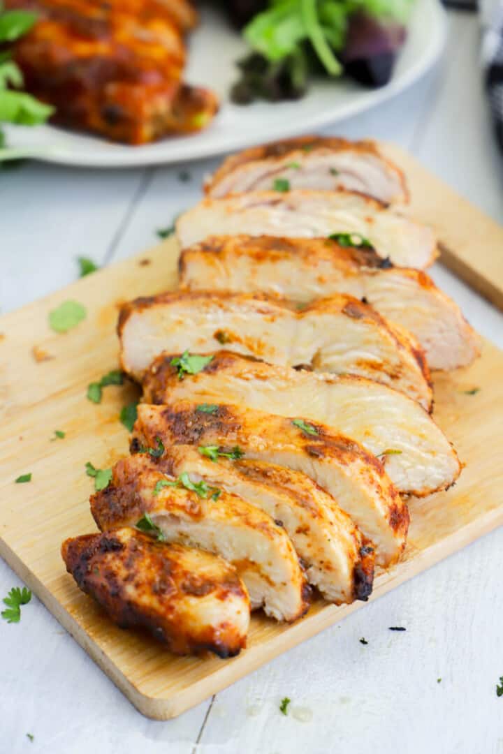 grilled chicken breast sliced on wooden cutting board.
