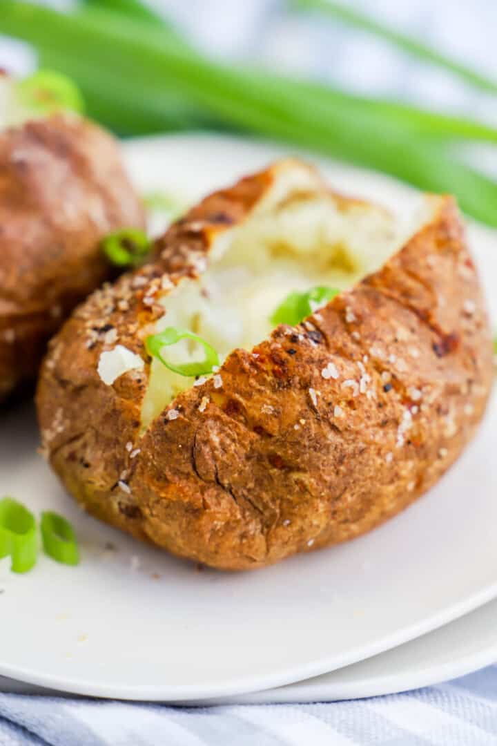 air fryer baked potato sliced open on white plate.