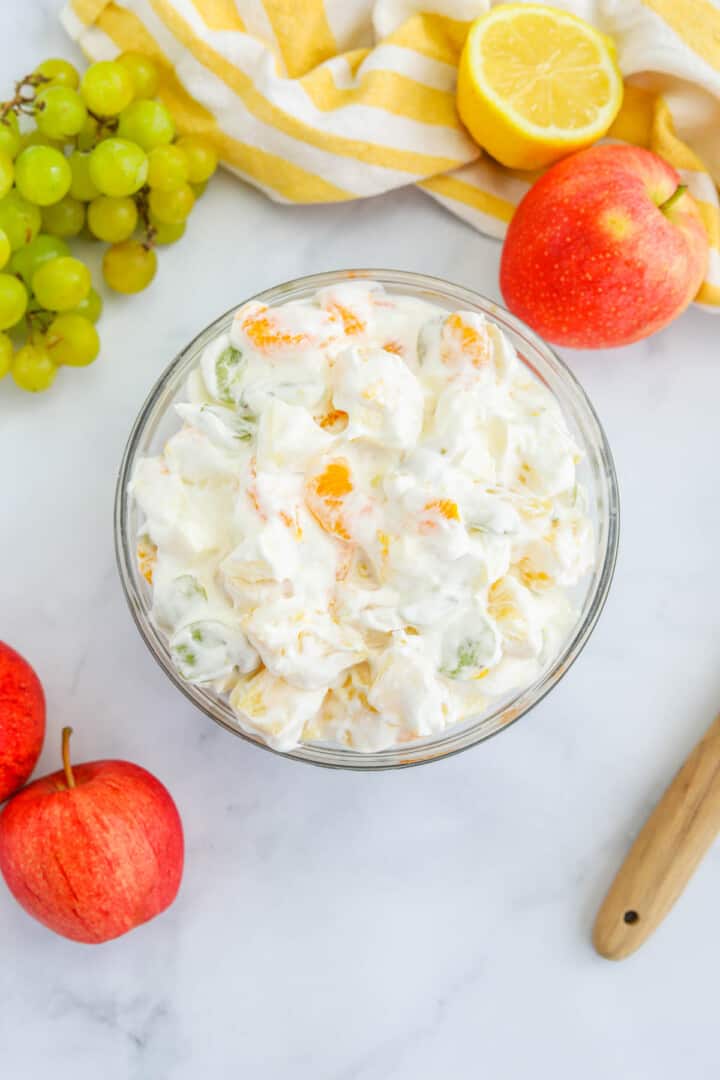 Creamy Fruit Salad in glass bowl with fruit around it.