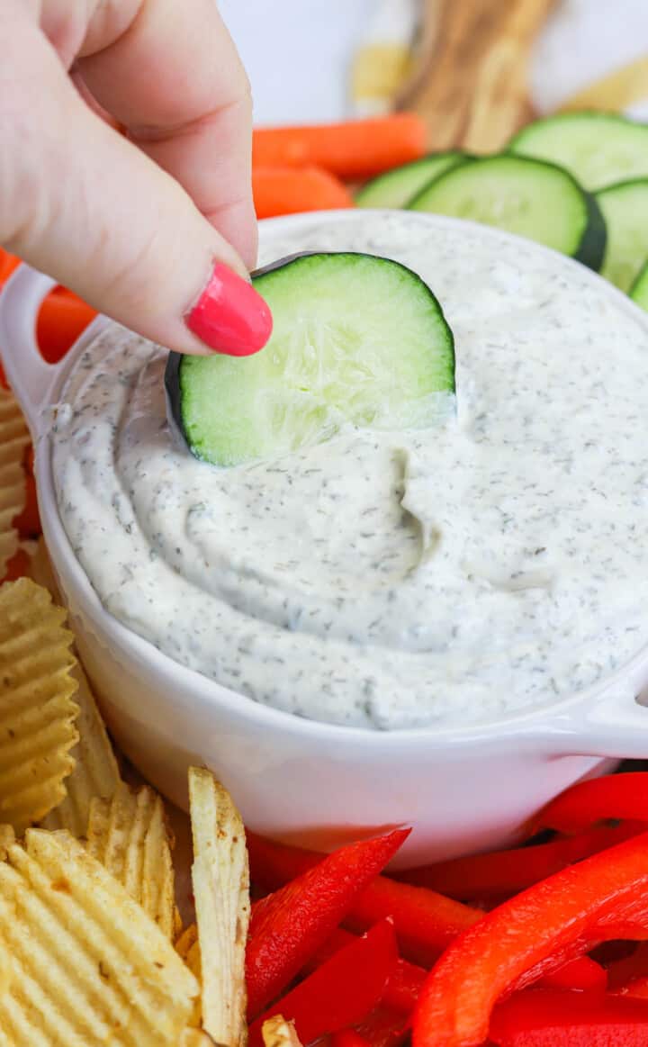 dipping cucumber slice in dill dip.