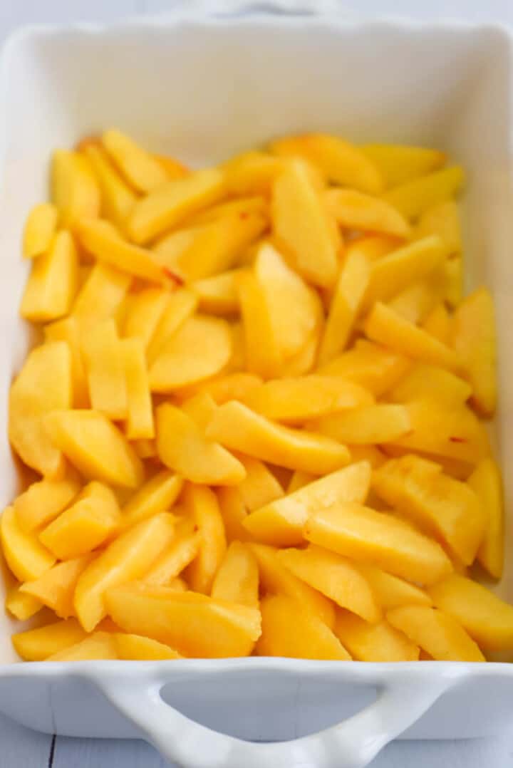 slices peaches in the bottom of a baking dish.