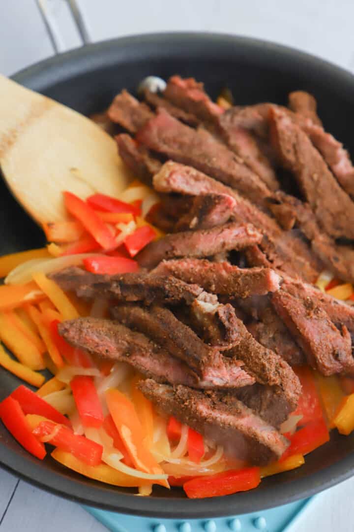 adding cooked steak to the peppers and onions in the skillet.