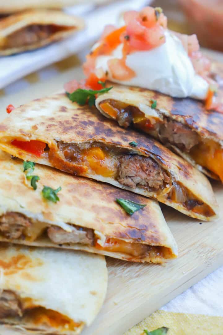 steak quesadilla sliced on wooden board with sour cream and salsa.
