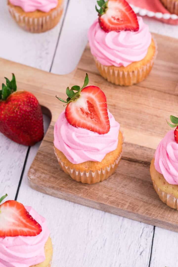top down view of strawberry cupcakes on wooden serving board.