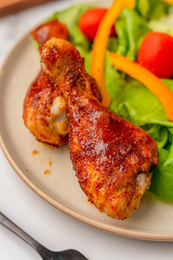 closeups of BBQ drumsticks on plate with a salad.