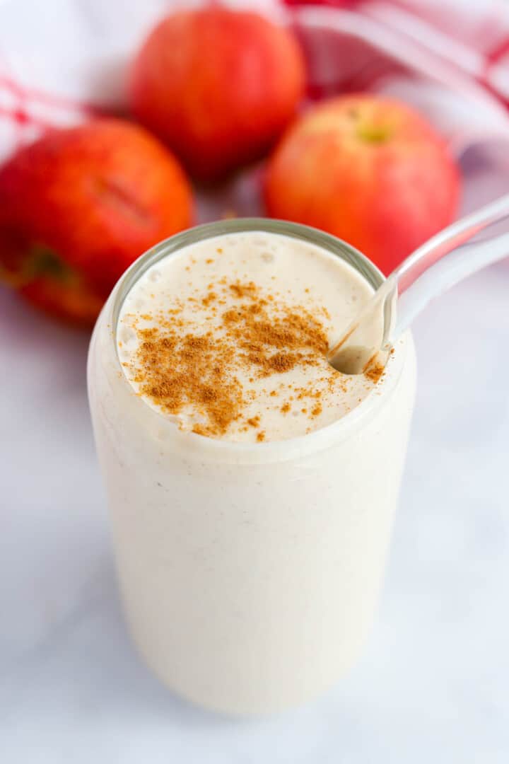 Apple Pie Smoothie in tall glass with apples in background.