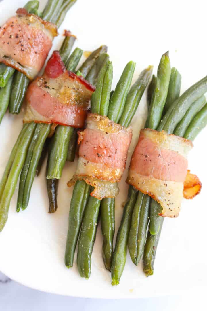 Closeup of bacon wrapped green beans on white plate.
