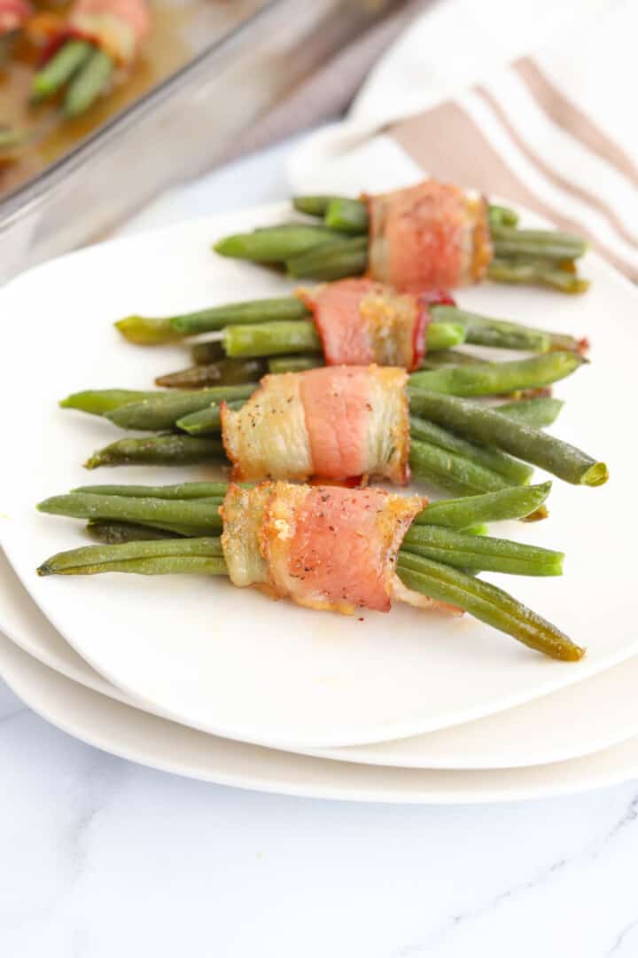 bacon wrapped green beans on stacked white plates.