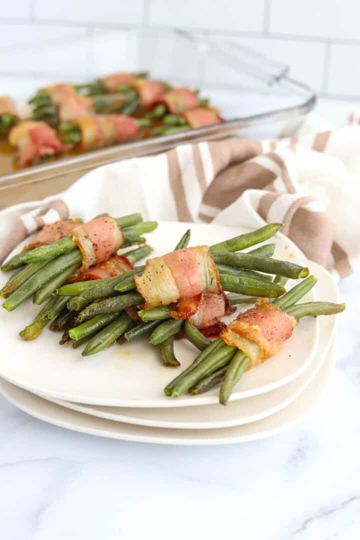 Bacon Wrapped Green Beans stacked on top of each other on white plate.