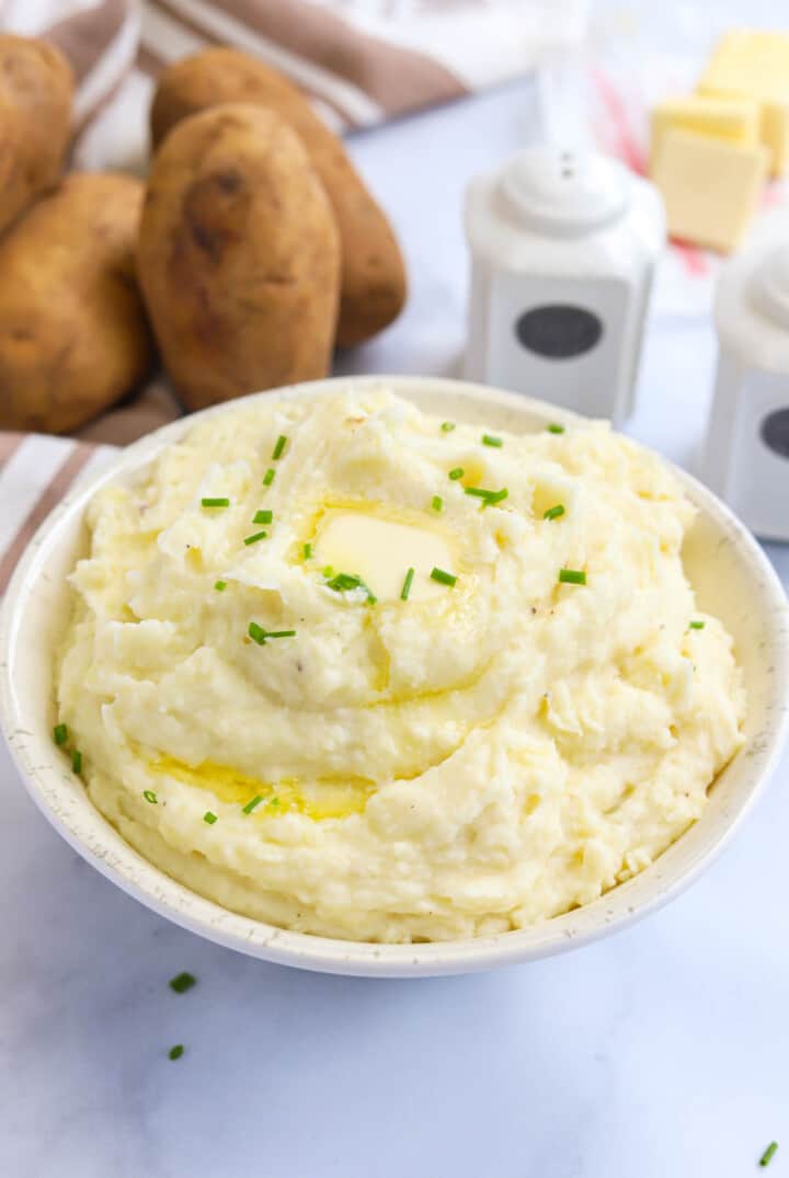 Garlic Mashed Potatoes in white bowl topped with chives and butter.