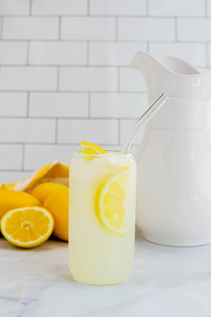 homemade lemonade on counter with lemons and pitcher behind it.