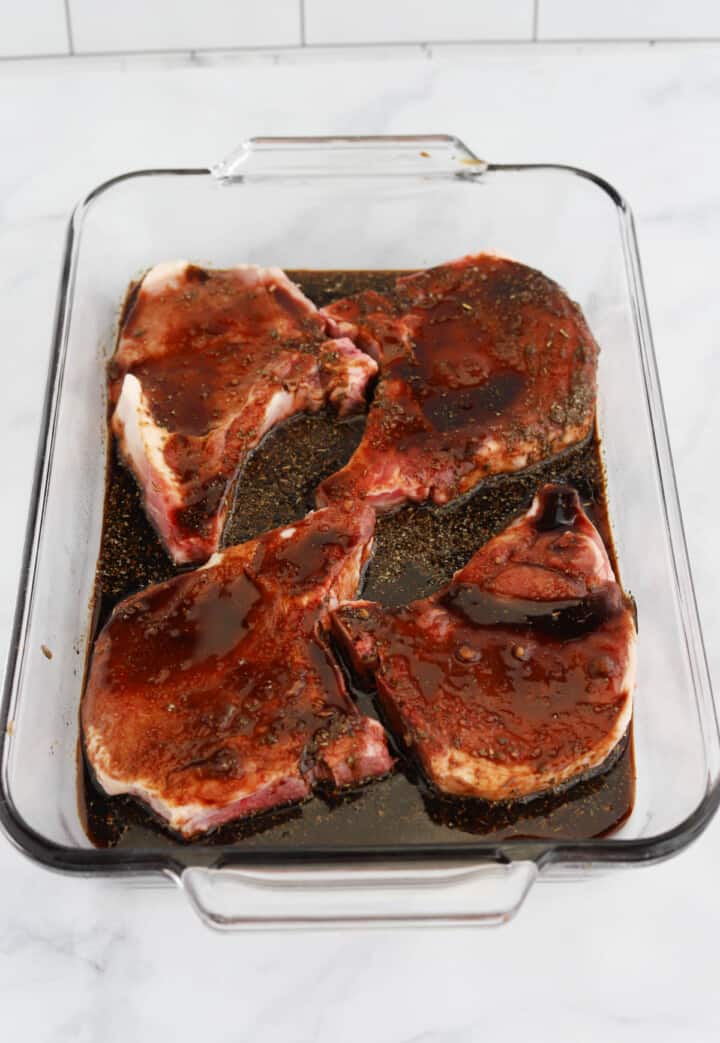 pork chops covered in marinade in baking dish.