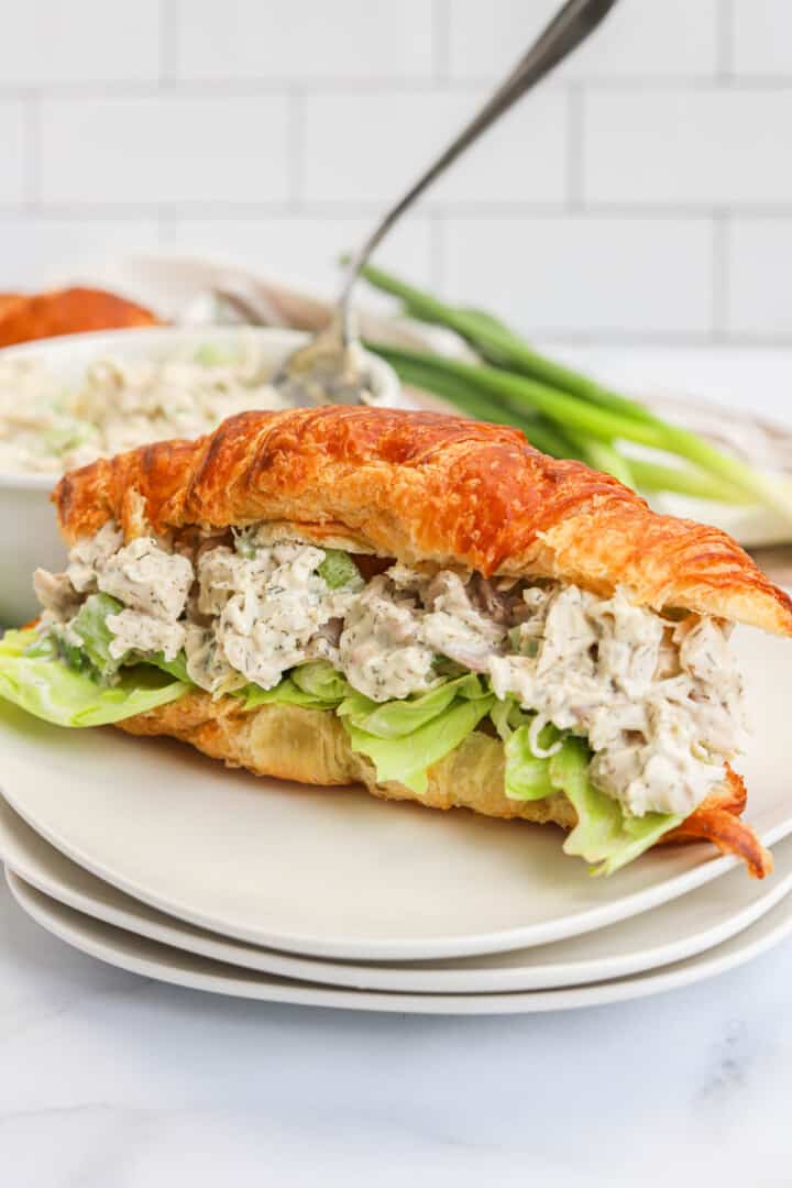 Turkey Salad on croissant on stacked white plates.