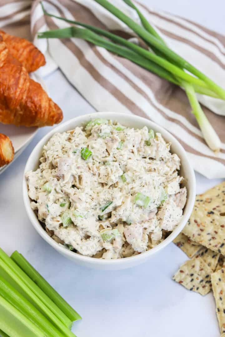 turkey salad in white bowl with croissants and celery on the side.