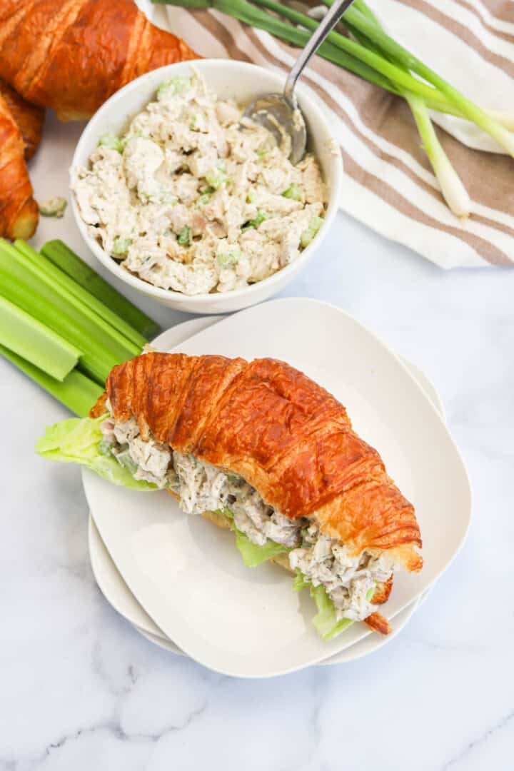 turkey salad served on croissant on white plate.