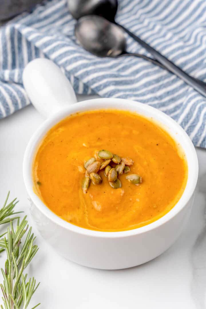 butternut squash soup in white bowl with pumpkin seeds on top.