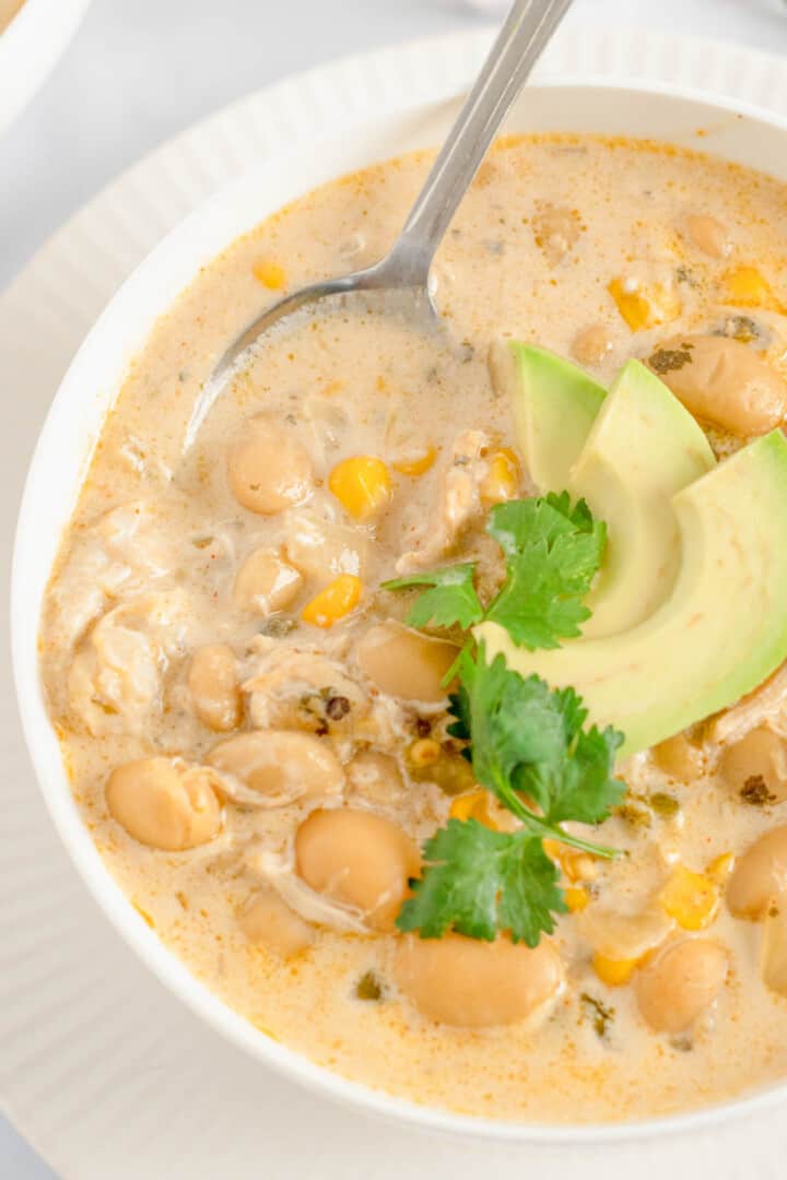 closeup of chili in white bowl with spoon and avocado slices.