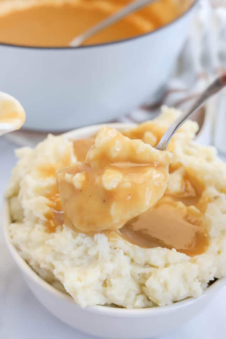 scooping the mashed potatoes topped with gravy out of bowl.