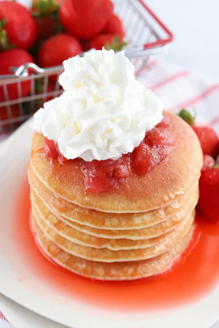 stack of pancakes with strawberry syrup and whipped cream.