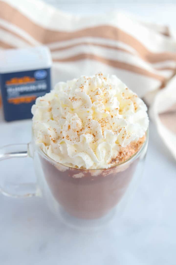 closeup of hot chocolate in clear mug topped with whipped cream.