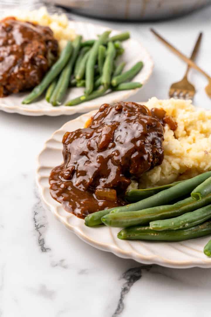 closeup of easy Salisbury steaks on plate with mashed potatoes and green beans.