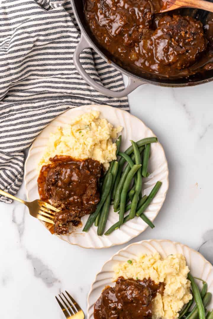 Easy Salisbury Steaks on plates with the skillet in the background.