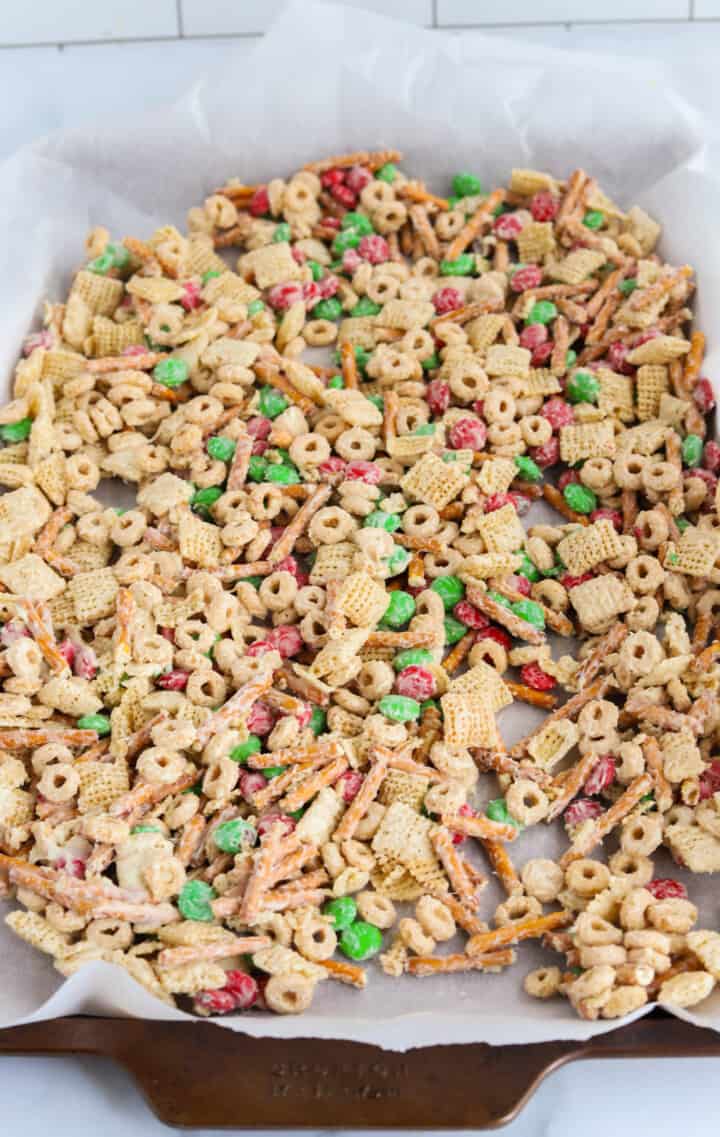 Christmas Chex Mix laid out on parchment covered baking sheet to dry.