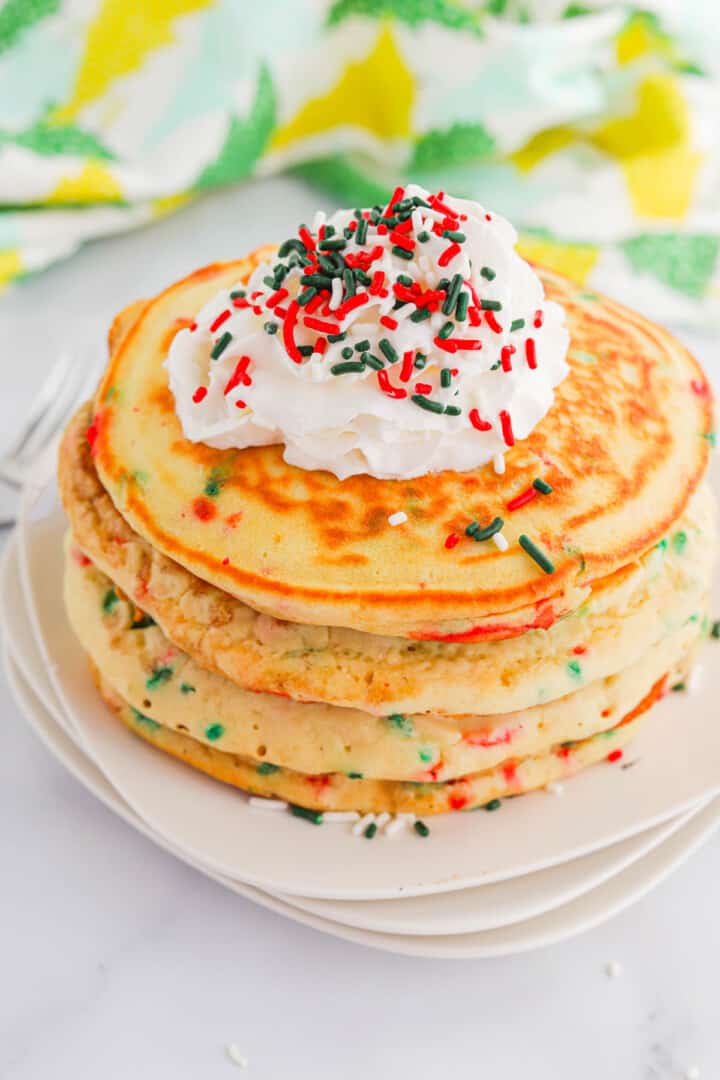 Christmas Pancakes stacked on white plates topped with whipped cream.