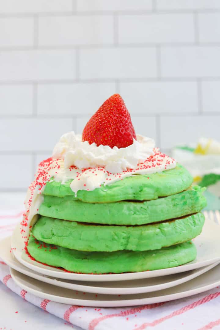 Grinch Pancakes stacked and topped with icing and a strawberry.