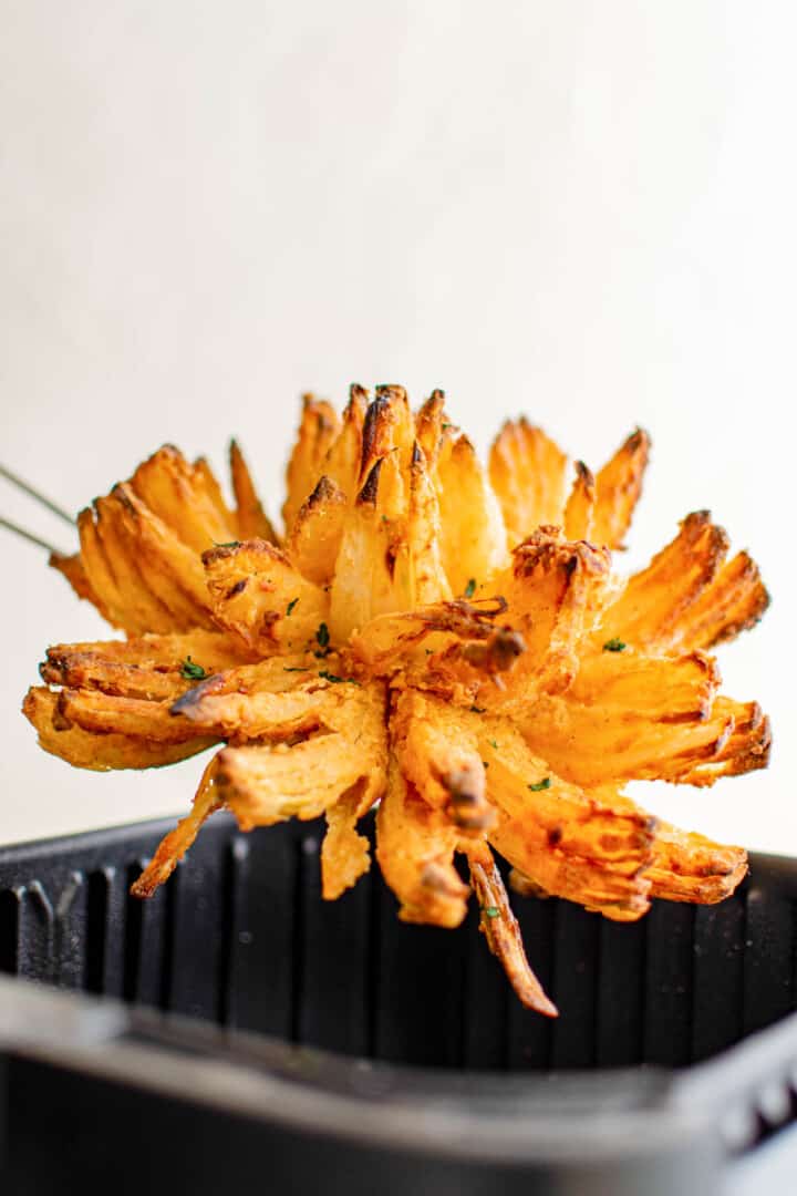 taking air fryer blooming onion out of the air fryer basket.