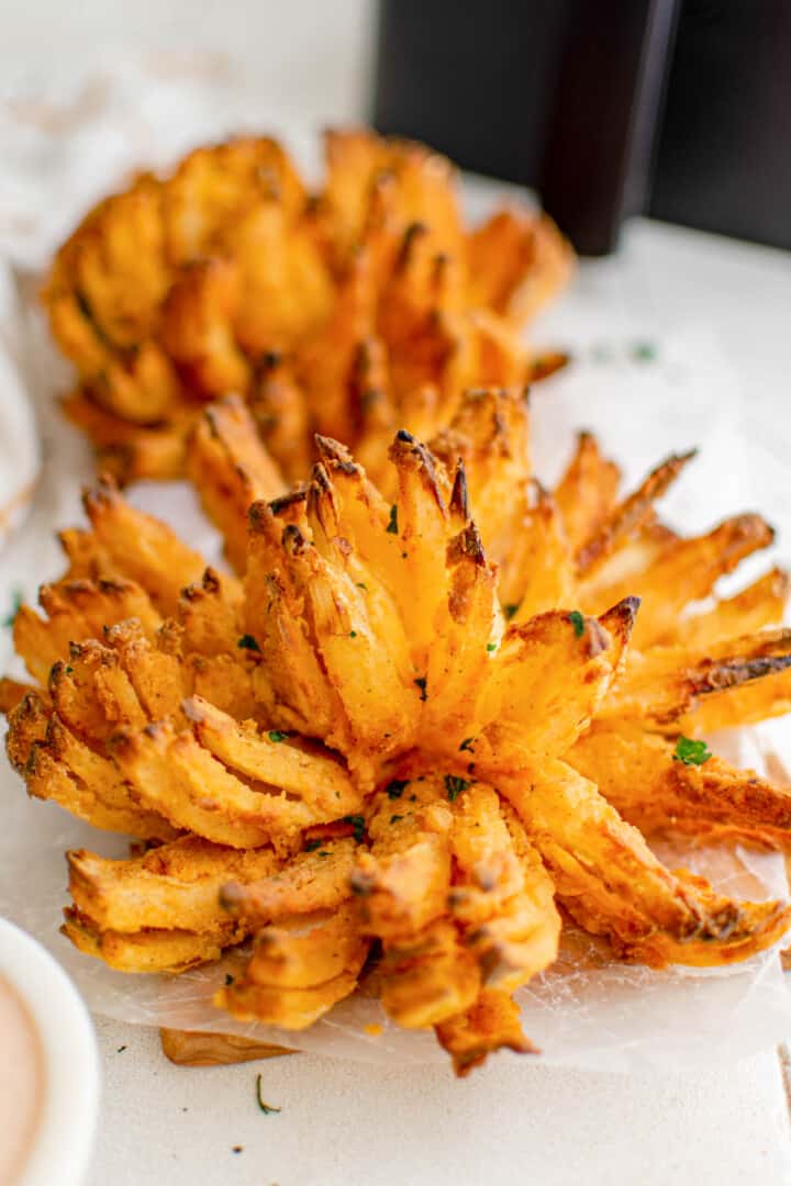 Two Air Fryer Blooming Onions on serving board with parchment paper.