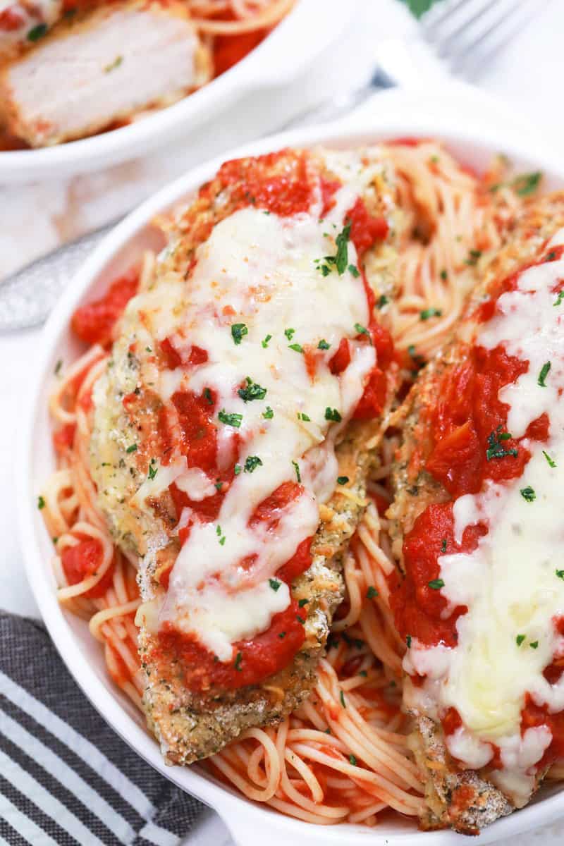 Baked Chicken Parmesan in white bowl on top of spaghetti.