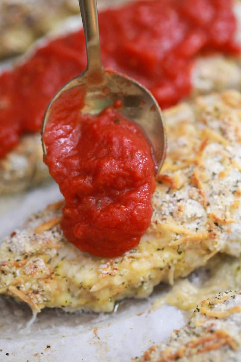 adding marinara to the top of the chicken breast.