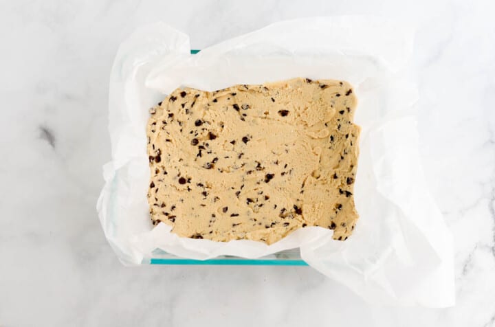 the raw cookie dough pressed into a baking dish with parchment paper.