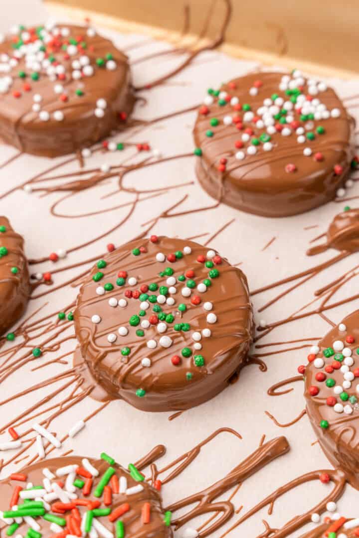 closeup of chocolate covered Oreos drying on parchment paper topped with sprinkles.