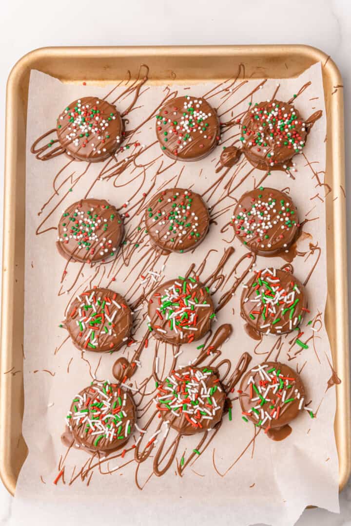chocolate covered Oreos drying on parchment paper topped with sprinkles.