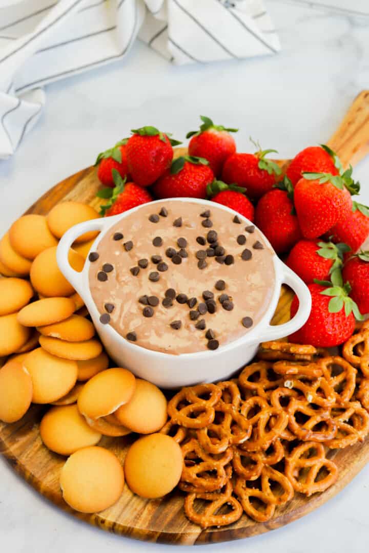 serving the brownie batter dip on wooden board with vanilla wafers, strawberries, and pretzels.
