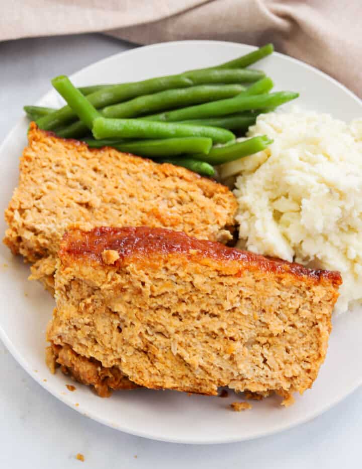 Chicken Meatloaf on white plate with green beans and mashed potatoes.