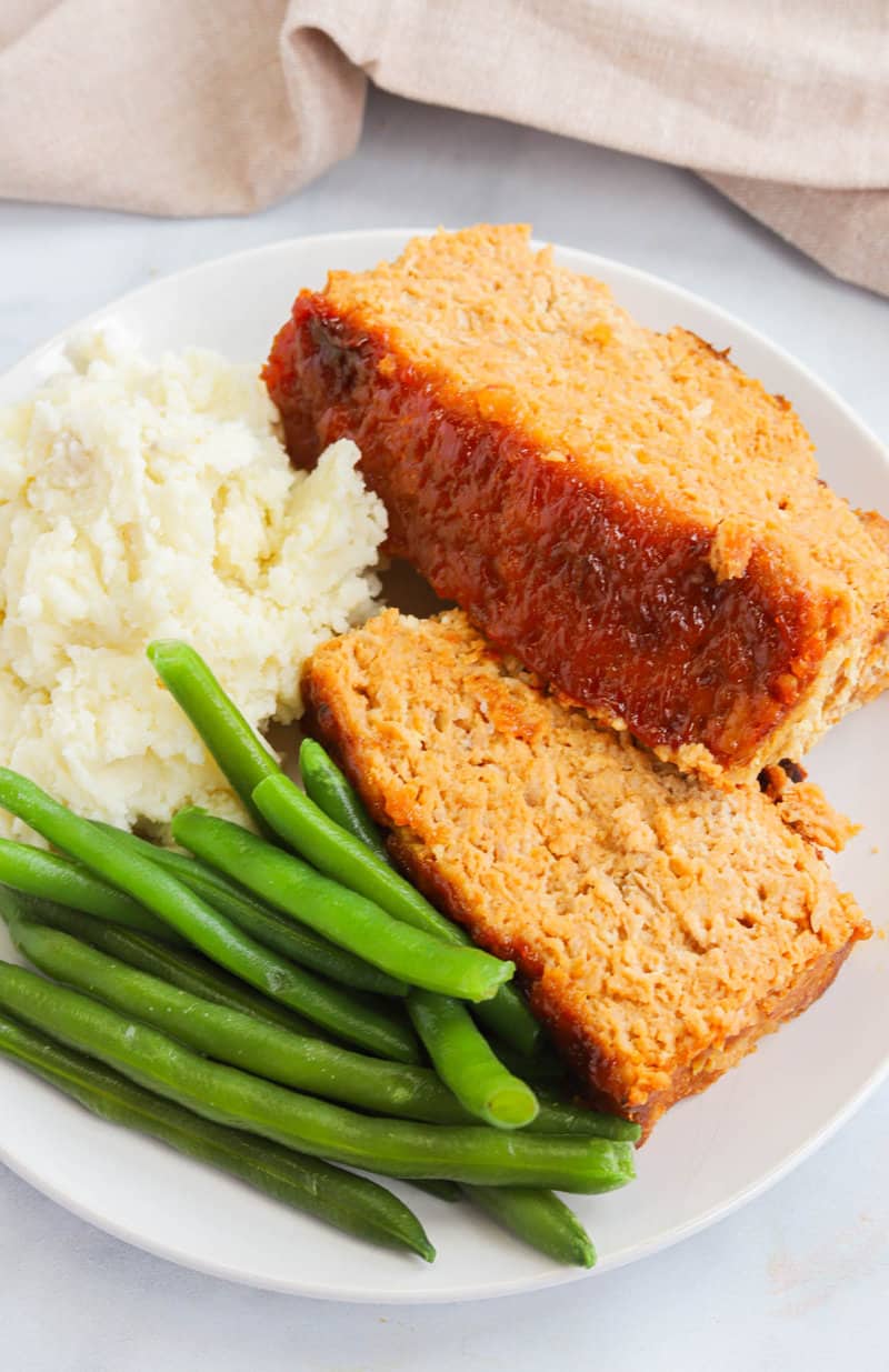 slices of meatloaf on plated with green beans and mashed potatoes.