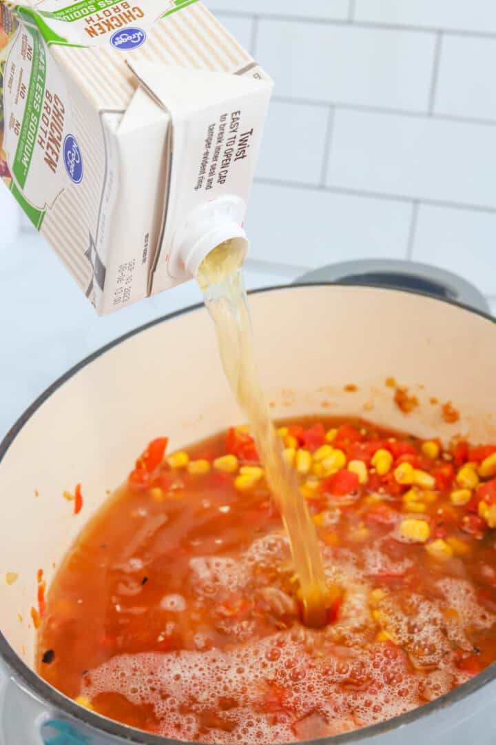 adding broth and other ingredients to large pot for soup.