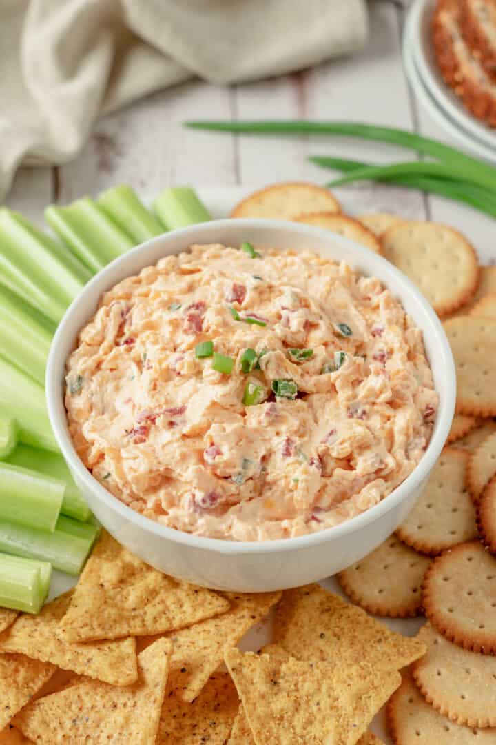 Pimento Cheese Dip in white bowl with crackers, chips and celery to dip.