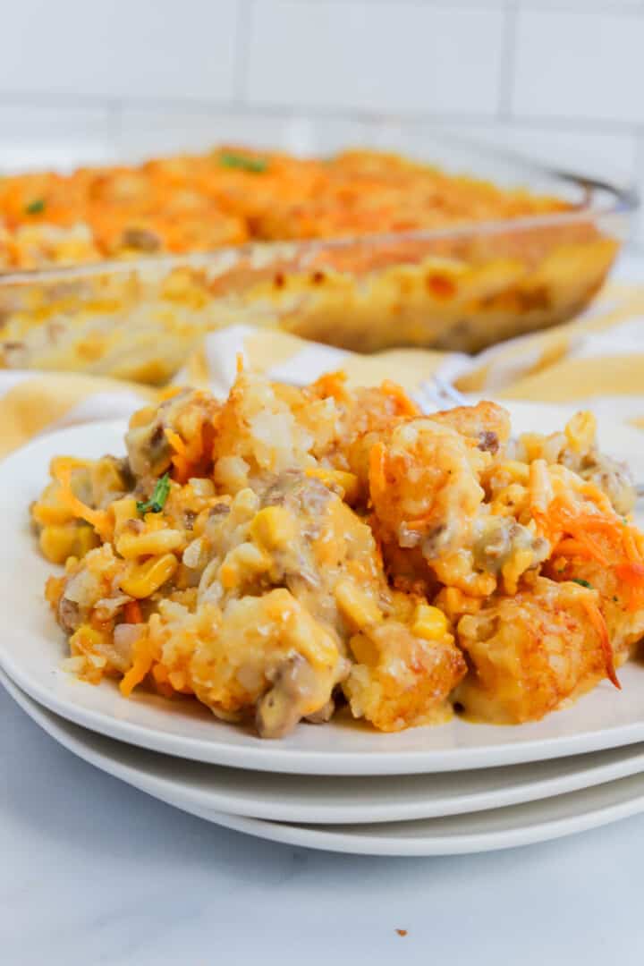 Tater Tot Casserole on stacked white plates with full casserole in background.