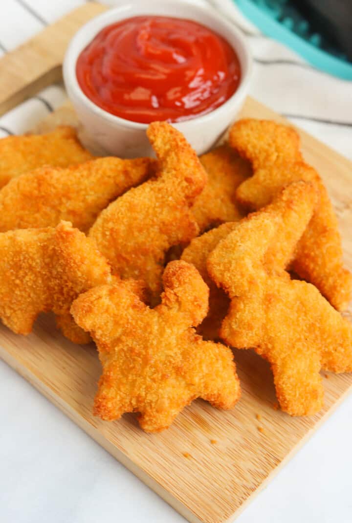 Air Fryer Dino Nuggets on wooden serving board with cup of ketchup.