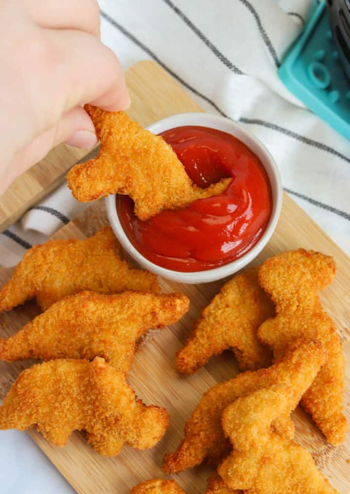 dipping a dino nugget into ketchup.