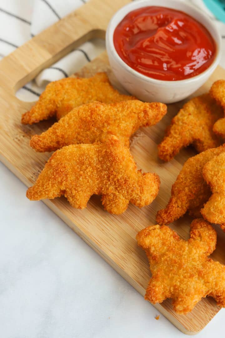 dino nuggets on wooden serving board with ketchup.
