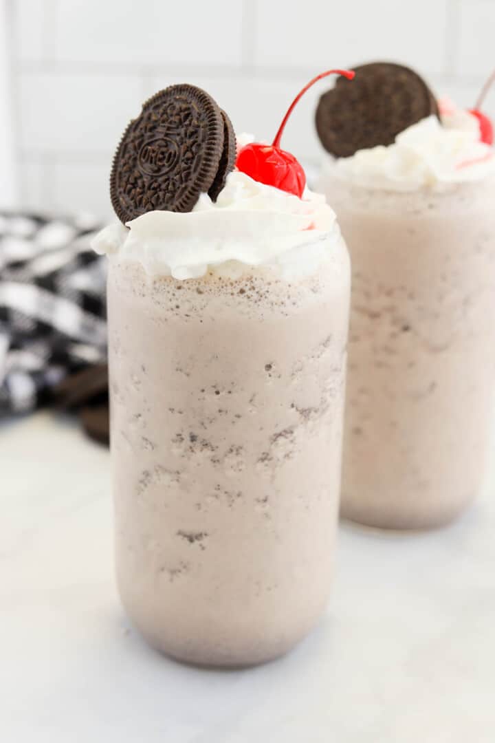 Oreo Milkshake in glass topped with whipped cream, an Oreo cookie and maraschino cherry.